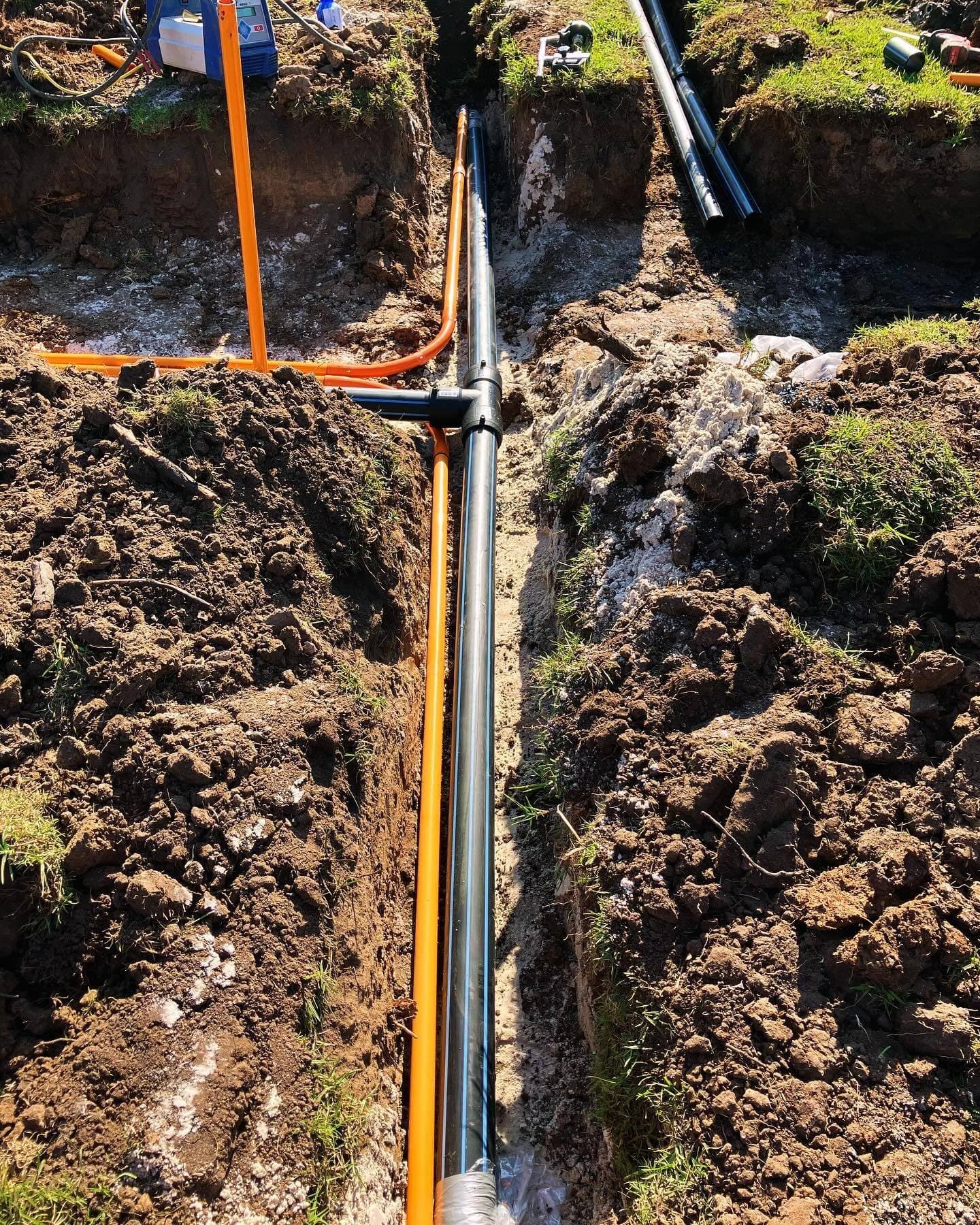 Trench showing the 90 mm HDPE mainline installed alongside orange electrical conduit