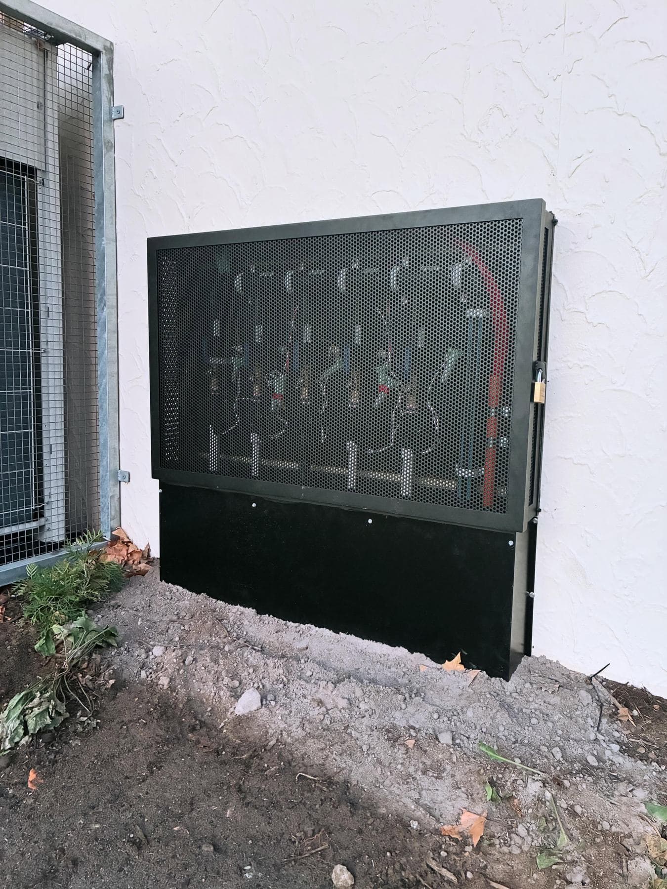 Perforated metal security enclosure protecting the valve manifold against an external wall