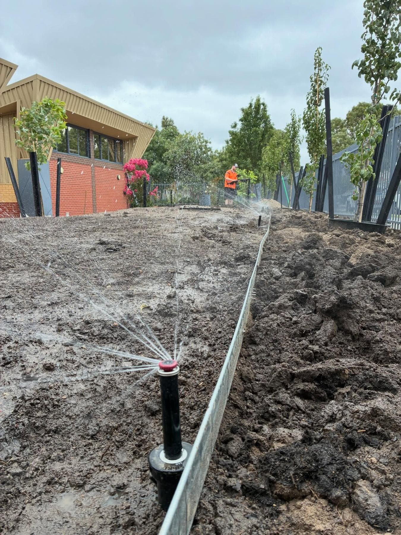Spray irrigation operating during testing beside a school building